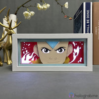 Boite lumineuse Aang Avatar cadre blanc éclairé lumière douce, motif flammes et flèche bleue visible, posée sur bureau