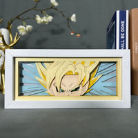 Boite lumineuse Goku Super Saiyan posée sur bureau, cheveux blonds dressés en papier découpé sur fond bleu ciel