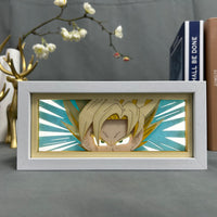 Boite lumineuse Goku Super Saiyan allumée bleu turquoise, visage déterminé en papier découpé avec rayons d'énergie