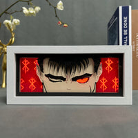 Boite lumineuse Guts Berserk cadre blanc, gros plan visage avec oeil rouge incandescent et symboles dorés sur fond rouge
