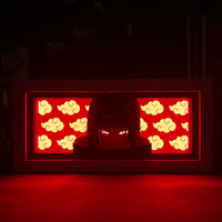 Boite lumineuse Itachi allumée dans le noir rouge intense portrait ninja yeux rouges fond nuages Akatsuki