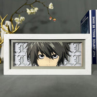 Boite lumineuse L Lawliet Death Note éteinte, cadre blanc avec lettres L décoratives sur fond gris clair, posée sur bureau