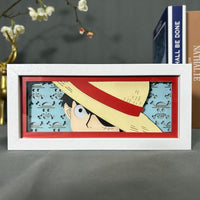 Boite lumineuse Luffy One Piece, chapeau de paille emblématique rouge et regard déterminé sur fond bleu avec têtes de mort