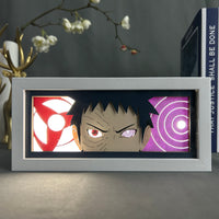 Boite lumineuse Obito Naruto allumée, sharingan rouge lumineux et rinnegan violet rétroéclairé posée sur bureau