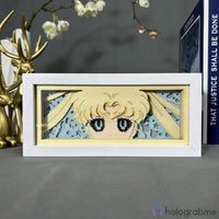 Boite lumineuse Sailor Moon en cadre blanc, yeux et tresses iconiques du personnage éclairés en jaune doux, posée sur un