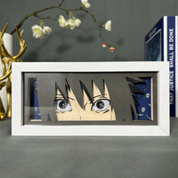 Boite lumineuse Sasuke Naruto éteinte, regard intense encadré de motifs bleus Uchiha posée sur un bureau