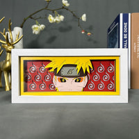 Boite lumineuse Naruto cadre blanc avec portrait du ninja fond rouge et tourbillons, posée sur bureau