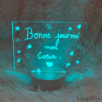 Lampe personnalisée turquoise avec message 'Bonne journée mon cœur' entouré d'étoiles et cœurs, posée sur fourrure blanche