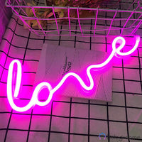 Néon LED inscription love en cursive rose fuchsia posé sur une grille de présentation blanche
