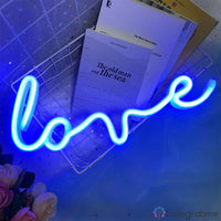 Néon LED inscription love en cursive bleu posé dans un panier métallique avec livres en décor