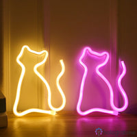 Deux néons LED chat silhouette jaune et rose posés au sol devant porte, décoration chambre cosy