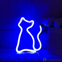 Néon LED chat silhouette bleu électrique posé sur socle avec fleurs blanches, décoration chambre