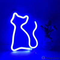 Néon LED chat silhouette bleu électrique posé sur surface avec vase de fleurs, ambiance chambre nuit