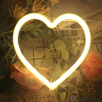 Néon LED cœur blanc chaud posé parmi des fleurs roses séchées sur grille déco, ambiance romantique