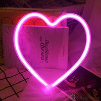 Néon LED cœur rose fuchsia posé avec livre vintage sur fond tissu, décoration chambre romantique