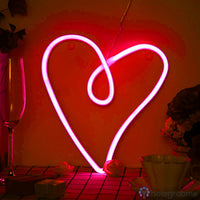 Néon LED cœur rose vif accroché au mur orange, posé sur table avec verre à champagne et fleurs, ambiance romantique