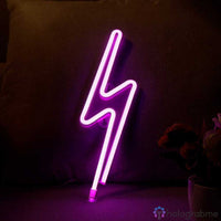 Néon LED éclair rose fuchsia posé sur un canapé sombre, décoration chambre ado ou salon ambiance rose vif