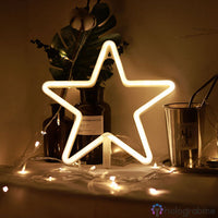 Néon LED étoile blanc chaud sur pied posé sur un meuble avec guirlande lumineuse et plante, déco salon cosy