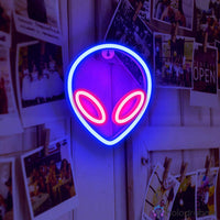 Néon LED alien bleu et rouge accroché sur mur avec polaroids et photos épinglées, décoration chambre ado tendance