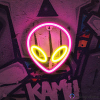 Néon LED alien rose fuchsia et jaune avec grands yeux lumineux accroché sur mur graffiti, décoration chambre ado