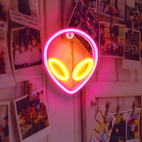 Néon LED alien rose et jaune accroché sur mur recouvert de polaroids et photos, décoration chambre ado originale