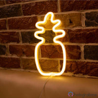 Néon LED ananas blanc chaud posé contre mur de briques rouges, ambiance estivale décoration intérieur
