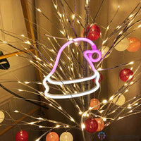 Néon LED bonnet de Noël rose et blanc accroché dans un décor de branches lumineuses dorées