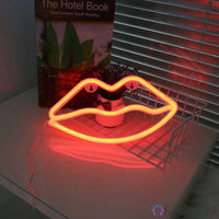 Néon LED bouche lèvres orange-rouge posé sur un bureau avec des livres, décoration chambre originale