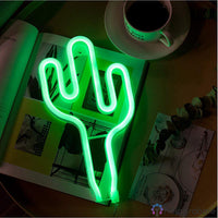 Néon LED cactus vert posé sur un livre ouvert avec une tasse de café, décoration bureau décontractée