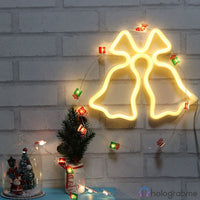 Néon LED cloches de Noël blanc chaud accroché au mur, entouré de guirlandes cadeaux colorées et d'un sapin miniature