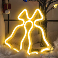 Néon LED cloches de Noël blanc chaud posé dans décor hivernal avec boules et arbre enneigé