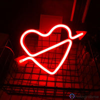 Néon LED cœur cupidon rouge lumineux avec flèche, posé dans un panier métallique, fond sombre