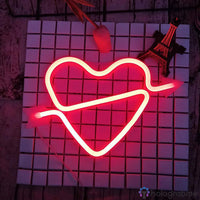 Néon LED cœur cupidon rouge avec flèche posé à plat sur surface carrelée, ambiance romantique