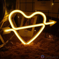 Néon LED cœur cupidon blanc chaud avec flèche posé sur sol doux, lumière dorée romantique