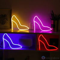 Quatre néons LED escarpin talon haut jaune, rose, bleu et rouge posés sur des meubles, déco chambre