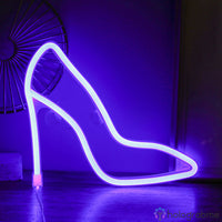 Néon LED escarpin talon haut violet posé sur un parquet sombre avec éventail mural, ambiance chic