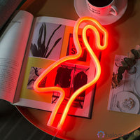 Néon LED flamant rose orange-rouge posé sur des magazines sur une table basse, style café moderne