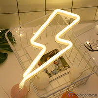Néon LED éclair blanc chaud posé dans panier grillage avec accessoires déco, ambiance bureau tendance