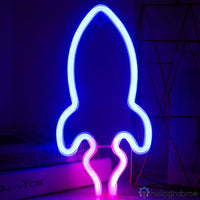 Néon LED fusée bleu électrique sur pied posé devant des livres, décoration bureau chambre ambiance spatiale