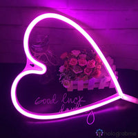 Néon LED grand cœur rose fuchsia posé près d'un bouquet de roses sur surface réfléchissante