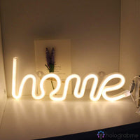 Néon LED inscription home blanc chaud en écriture cursive posé sur une étagère avec fleurs séchées, déco cosy