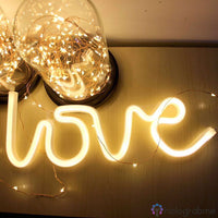 Néon LED love blanc chaud en script posé sur un meuble déco avec des ampoules dorées en fond