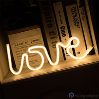 Néon LED love blanc chaud en cursif posé dans une étagère avec des livres, ambiance salon cosy
