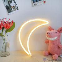 Néon LED lune croissant blanc chaud posé sur bureau avec peluche cochon rose, décoration chambre enfant