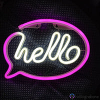 Néon LED hello en cursive blanche dans bulle de dialogue rose, accroché au mur fond sombre