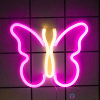 Néon LED papillon rose fuchsia et jaune doré accroché sur mur carrelé gris, décoration murale chambre ou couloir