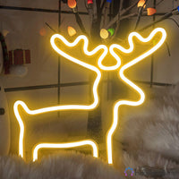 Néon LED renne blanc chaud posé sur une surface enneigée avec guirlandes et sapin, décoration Noël lumineuse