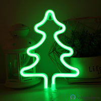 Néon LED sapin vert brillant posé sur un bureau avec des objets déco, ambiance chambre tamisée