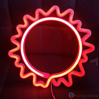 Néon LED soleil rouge-orange aux rayons lumineux posé contre tissu bordeaux, décoration murale chambre tendance