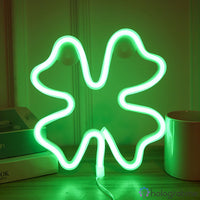 Néon LED trèfle à quatre feuilles vert lumineux posé sur un bureau à côté de livres et d'une tasse